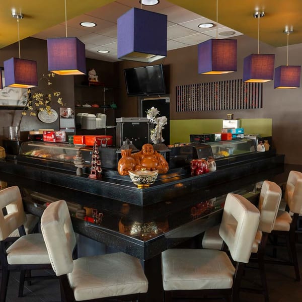Sushi bar at Tea Tree Asian Bistro with purple hanging lights, a Buddha statue, and bar stools.