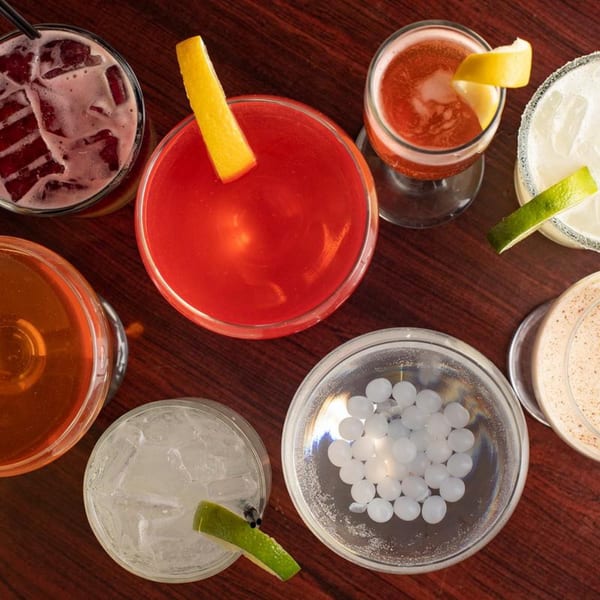 An overhead view of various colorful cocktails and drinks on a dark wooden table.