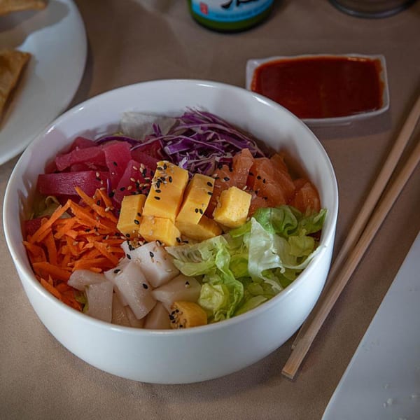 Colorful Tea Tree Asian Bistro poke bowl with tuna, salmon, egg, and vegetables, with chopsticks and sauce.
