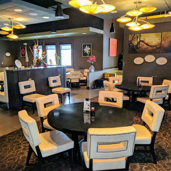 The Tea Tree Asian Bistro dining room features dark tables, cream chairs, and Asian-inspired decor under warm lighting.