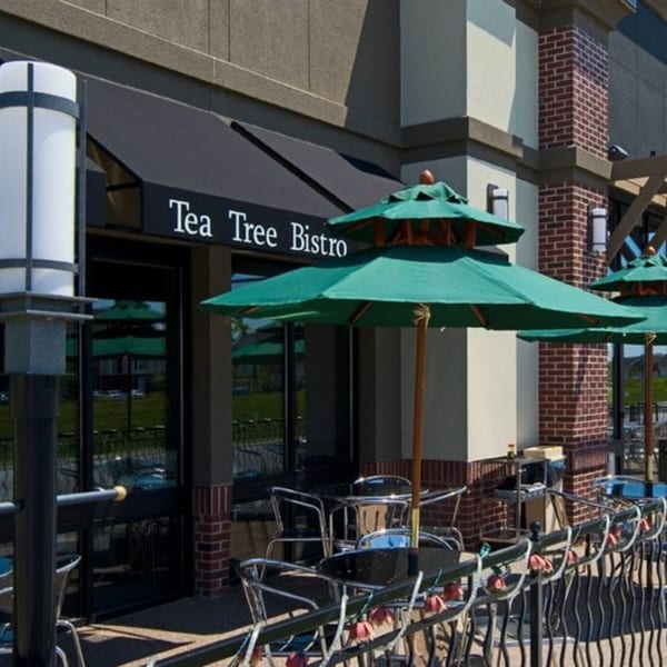 Exterior of Tea Tree Asian Bistro with a black awning, green umbrellas, and outdoor seating.