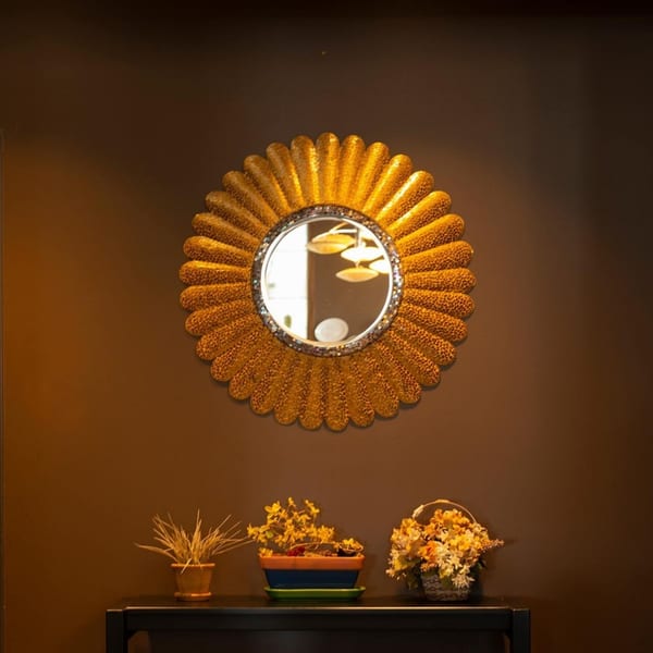 A golden sunburst mirror hangs above a dark table with potted plants and a flower basket.
