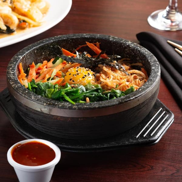 A stone bowl of colorful bibimbap with a raw egg yolk, seaweed, and vegetables, with sauce on the side.