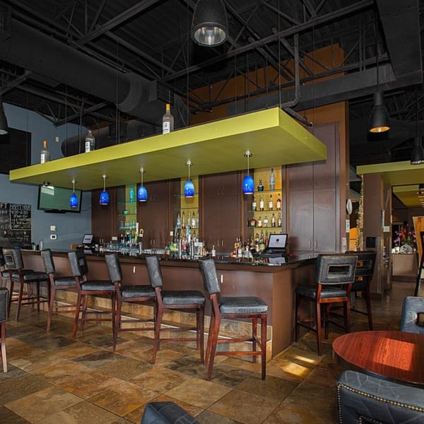 Tea Tree Asian Bistro's bar area with a long counter, bar stools, and bottles of liquor.