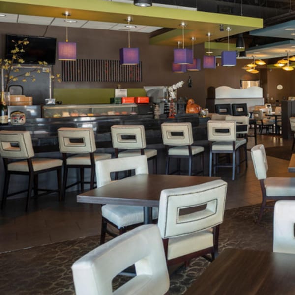 Modern Asian bistro interior with a sushi bar, white chairs, and purple pendant lights.