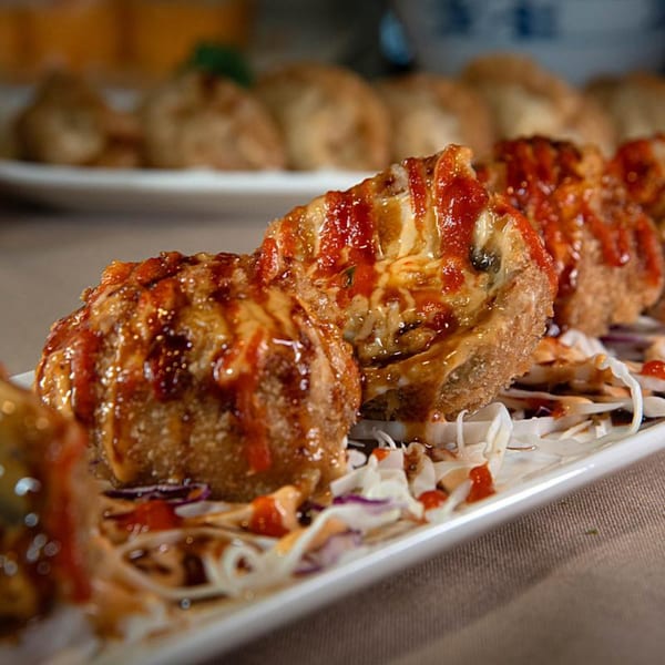 Crispy fried Asian-fusion dumplings topped with melted cheese and red sauce on a white plate.