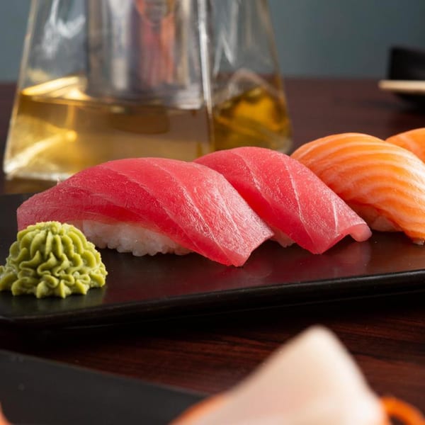Close-up of fresh tuna and salmon nigiri sushi with wasabi on a dark plate.